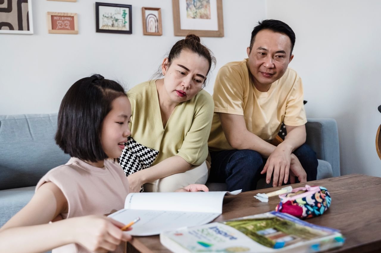 Parents assisting daughter with her homework in a cozy living room setting.